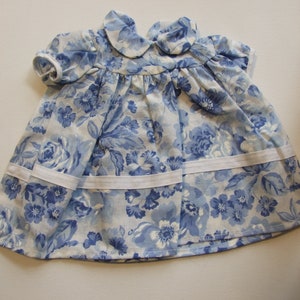 Peut inclure: Robe de bébé avec un motif floral bleu sur fond blanc. La robe a des manches courtes, un col Claudine et une bordure blanche. Le tissu est une matière légère et douce. Idéale pour un bébé.