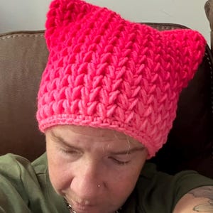 May include: A pink crocheted hat with a pointed top and a gradient of color from dark pink to light pink.