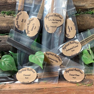 May include: Assortment of incense sticks in clear plastic bags with brown paper labels. The labels have the text "Mystical OutPest" and the name of each scent, including "Firewood", "Pine", "Balsam Fir", "Let's Go Camping", "Enchanted Forest", "Enchanted Oak", "Campfire", and "Forest Floor".