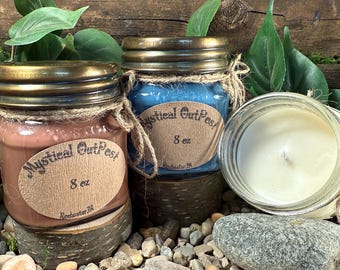 May include: Three 8 ounce glass jar candles with brown, blue, and white wax. The jars have gold lids and are tied with twine. The labels on the jars read "Mystical Outpost".