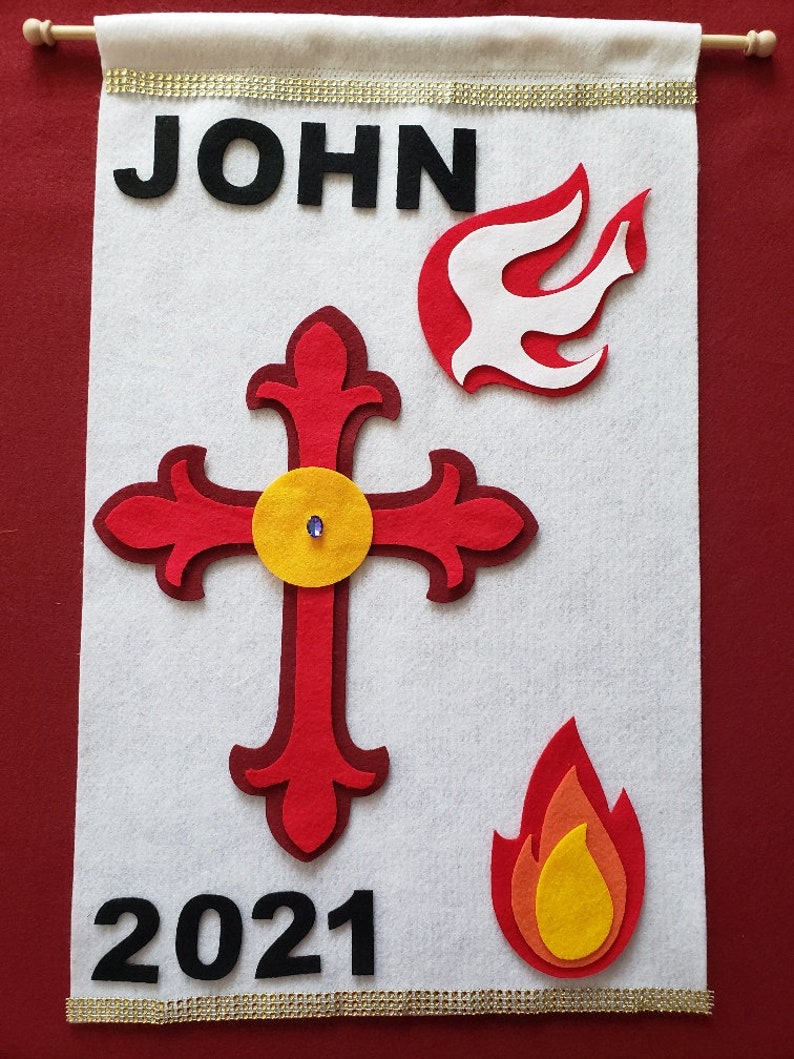 Pu&ograve; includere: Striscione in feltro bianco con il nome "JOHN" in lettere nere, l'anno "2021" in lettere nere, una croce rossa con un cerchio giallo al centro e due fiamme rosse con centri gialli.