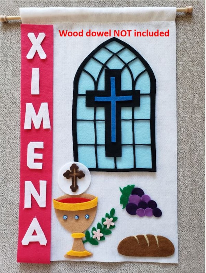 May include: A white felt banner with the name "XIMENA" in white letters on a red background. The banner also features a blue cross in a stained glass window, a chalice, a loaf of bread, and grapes. The text "Wood dowel NOT included" is written in red at the top of the banner.