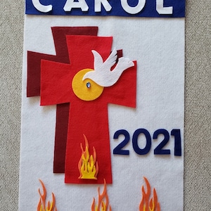 Pu&ograve; includere: Uno stendardo di feltro bianco con uno stendardo blu in alto che dice "CAROL 2021". Una croce di feltro rosso con una colomba bianca e un cerchio giallo &egrave; al centro. Ci sono tre fiamme arancioni in basso.