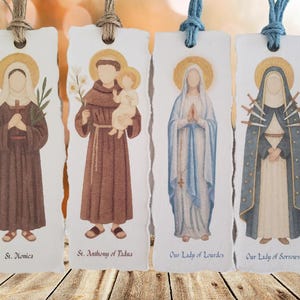 May include: Four watercolor bookmarks featuring religious figures. Each bookmark has a torn edge and a string for hanging. The figures include St. Monica, St. Anthony of Padua, Our Lady of Lourdes, and Our Lady of Sorrows. Each figure is depicted with a gold halo.