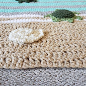 Peut inclure: Une sc&egrave;ne de plage en crochet avec un coquillage blanc, des tortues de mer vertes et des rayures bleues et blanches.