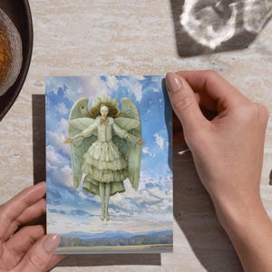 Hands holding a printed angel postcard over wood, demonstrating print at home use for printable Christmas angel paper dolls