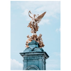 Op de afbeelding: Een gouden standbeeld van een gevleugelde figuur met een kroon, staande op een stenen monument. Het standbeeld wordt omringd door andere figuren, en het monument is versierd met ingewikkelde houtsnijwerk.