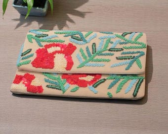 Può includere: Pochette beige con ricami floreali rossi e foglie verdi e blu. La pochette rettangolare ha una patta ripiegabile. Il ricamo dettagliato copre la parte anteriore della pochette.