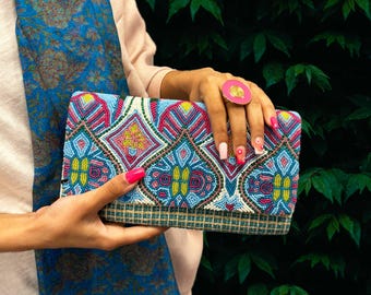 Può includere: Una pochette colorata con perline con un motivo geometrico in tonalità di blu, rosa, verde e giallo. La pochette ha una chiusura a lembo e una fodera in tessuto intrecciato.