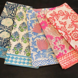 May include: Four folded fabric napkins with various floral and geometric patterns. The napkins display designs in blue, green, pink, and red on a white background. The patterns include stylized flowers and botanical motifs.