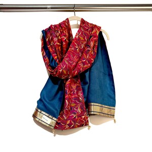 May include: A red and gold patterned scarf with a teal blue lining and gold trim. The scarf is hanging on a hanger.