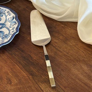 May include: A white ceramic mug with a black handle and the text "But First, Coffee" in a black, handwritten-style font. The mug is on a white surface.