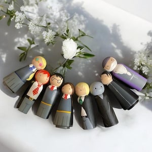 May include: A set of eight hand-painted wooden peg dolls dressed as characters from the Harry Potter series. The dolls are wearing robes and have various facial expressions.