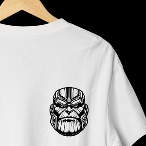 May include: White t-shirt featuring a black and white graphic of a character's face. The design is a detailed illustration with strong lines and shading, creating a bold visual impact. The shirt is hanging on a wooden hanger.