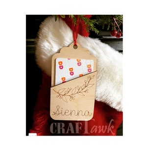 Puede incluir: Un porta tarjetas de regalo de madera con un recorte para una tarjeta de regalo. El porta tarjetas est&aacute; decorado con un dise&ntilde;o floral y el nombre "Sienna" est&aacute; grabado en la parte delantera. El porta tarjetas est&aacute; colgado de una cinta roja.