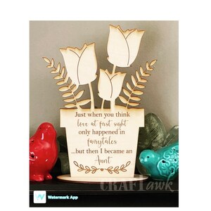 May include: Wooden floral decoration featuring tulip-shaped flowers and leafy accents. The text reads, "Just when you think love at first sight only happened in fairytales...but then I became an Aunt." Decorative item.