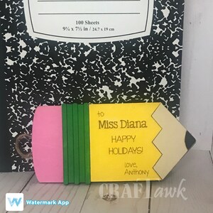 May include: A yellow and pink pencil-shaped wooden sign with a green eraser. The sign says "to Miss Diana Happy Holidays! Love, Anthony".
