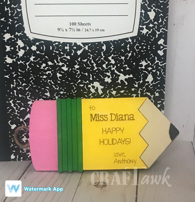 May include: A yellow and pink pencil-shaped wooden sign with a green eraser. The sign says "to Miss Diana Happy Holidays! Love, Anthony".