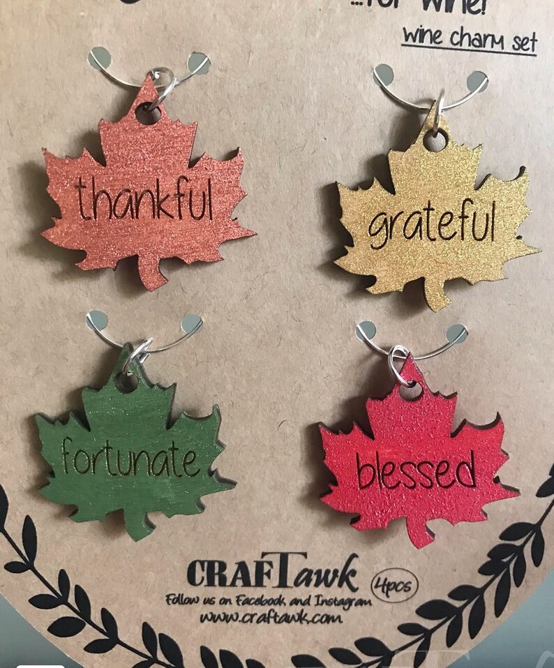 Puede incluir: Un conjunto de cuatro colgantes para vino con forma de hoja en colores oto&ntilde;ales: naranja, dorado, verde y rojo. Cada colgante tiene una palabra: "thankful", "grateful", "fortunate" y "blessed". El conjunto se presenta como un "wine charm set".