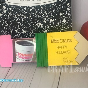 May include: A yellow pencil-shaped gift tag with the text "to Miss Diana Happy Holidays! love, Anthony" and a green and pink background. The tag is decorated with a Dunkin' Donuts gift card.