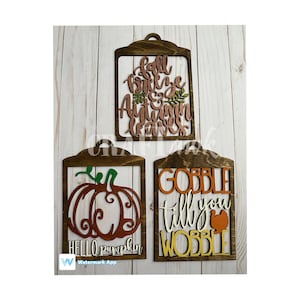 Puede incluir: Tres letreros de madera con diseños de otoño. El letrero de arriba dice "Fall breeze & Autumn leaves" en letras de cobre. El letrero de la izquierda dice "Hello pumpkin" con una silueta de calabaza. El letrero de la derecha dice "Gobble till you wobble" con una silueta de pavo.
