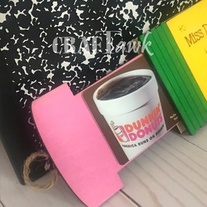 May include: A pink and brown wooden sign with a Dunkin' Donuts logo and the text "America Runs on Dunkin'" on it. The sign is propped up against a black and white notebook.