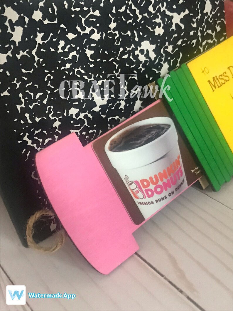 May include: A pink and brown wooden sign with a Dunkin' Donuts logo and the text "America Runs on Dunkin'" on it. The sign is propped up against a black and white notebook.