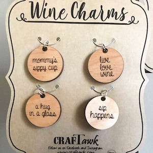 May include: Four wooden wine charms with different sayings. The charms are displayed on a wooden board with the text "Wine Charms" at the top. The sayings on the charms are "mommy's sippy cup", "live love wine", "a hug in a glass", and "sip happens".