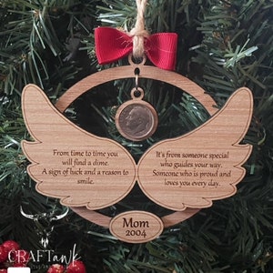 Könnte beinhalten: Holzengel-Anhänger mit einem Zehn-Cent-Stück, das daran hängt. Der Anhänger hat den Text "From time to time you will find a dime. A sign of luck and a reason to smile." und "It's from someone special who guides your way. Someone who is proud and loves you every day." Der Anhänger hat auch den Text "Mom 2004".