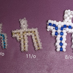 Op de afbeelding: Drie geperde kruisen in verschillende maten, waarbij het grootste kruis wit is met blauwe kralen, het middelste kruis helder is met gouden kralen en het kleinste kruis helder is met blauwe kralen. De kruisen zijn gemarkeerd met hun maat in kralen per inch: 8/0, 11/0 en 15/0.