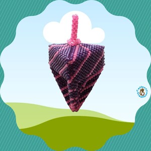 May include: A purple and pink beaded dreidel, a traditional Jewish spinning top, with a pink top. The dreidel is against a blue sky background with a green grassy hill in the foreground.