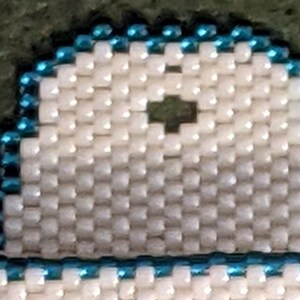K&ouml;nnte beinhalten: Ein wei&szlig;er Perlenanh&auml;nger mit blauem Rand. Der Anh&auml;nger hat ein kleines Loch in der Mitte.