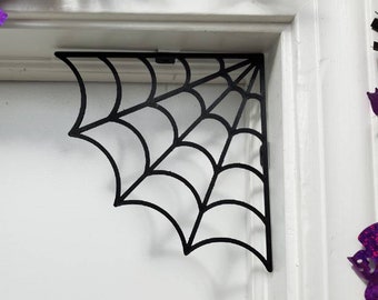 May include: Black metal spider web corner shelf bracket. The bracket is shaped like a spider web and is designed to be mounted in a corner.