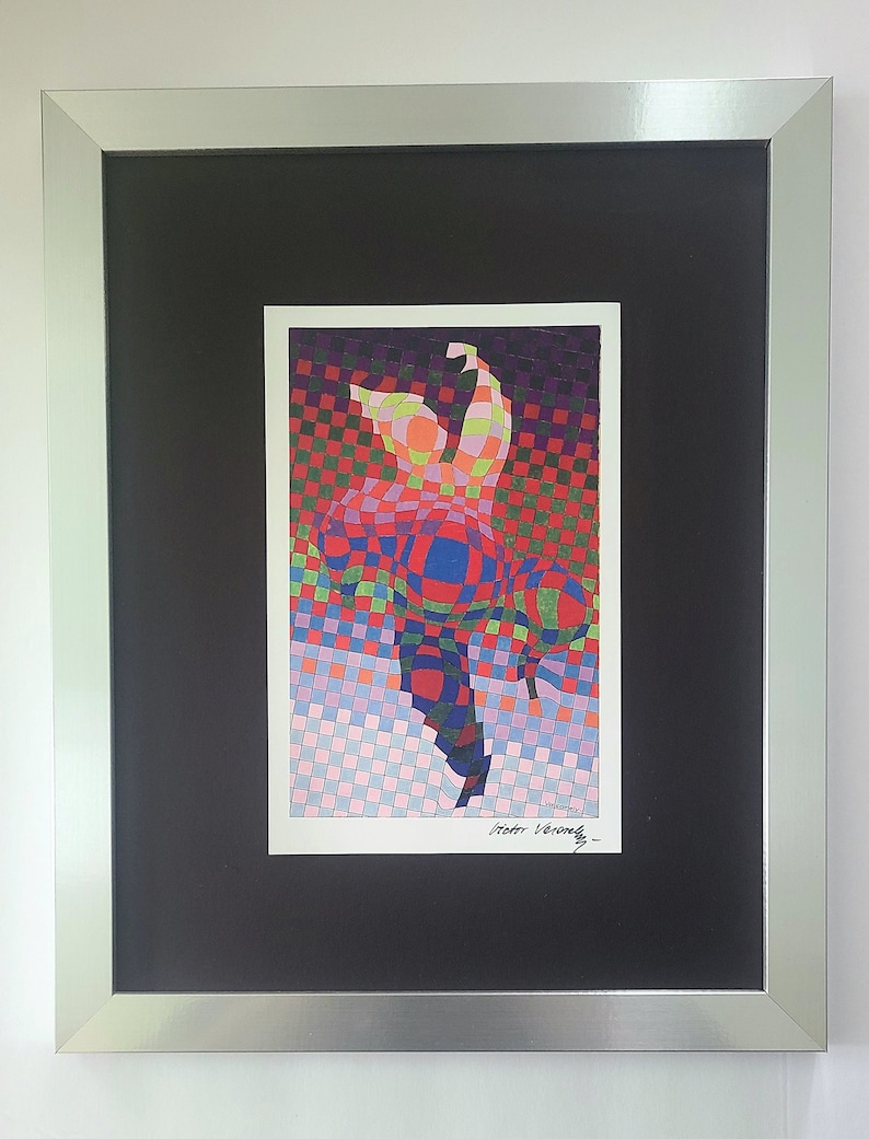 May include: A framed print of a colorful abstract art piece with a checkered background. The print is signed "Victor Vasarely" in the bottom right corner.