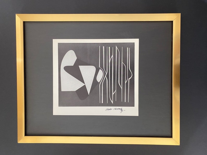 May include: A black and white abstract art print in a gold frame. The print features geometric shapes and lines. The artist's signature is visible in the bottom right corner.