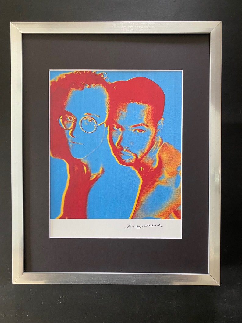 Puede incluir: Una impresi&oacute;n enmarcada de un retrato pop art de dos hombres, uno con gafas, en colores rojo, amarillo y azul. La impresi&oacute;n est&aacute; firmada "Andy Warhol".