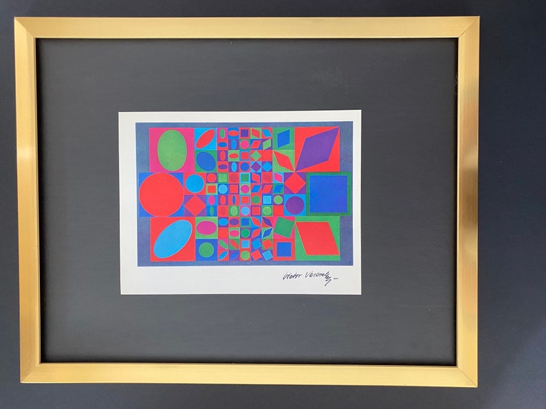 May include: A framed abstract art print with a geometric design featuring circles, squares, and triangles in shades of red, blue, green, and purple. The print is signed "Victor Vasarely" in the bottom right corner.
