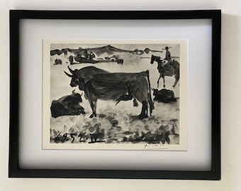 May include: Black and white print of a bull and a rider on horseback in a field. The print is signed "Picasso" in the bottom right corner and dated "6.5.52 IV" in the bottom left corner.