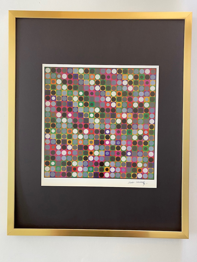 May include: A framed print of a colourful abstract artwork featuring a grid of squares and circles in various shades of red, green, blue, yellow, and white. The artist's signature, "Victor Vasarely", is visible in the bottom right corner.