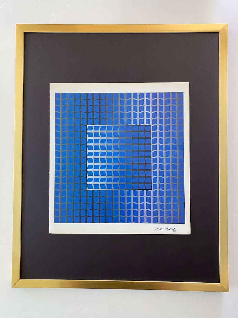 Puede incluir: Impresi&oacute;n art&iacute;stica abstracta en un marco dorado. La obra presenta un dise&ntilde;o geom&eacute;trico azul y plateado con un cuadrado dentro de un cuadrado. La impresi&oacute;n est&aacute; sobre un passe-partout negro, y el marco es dorado.