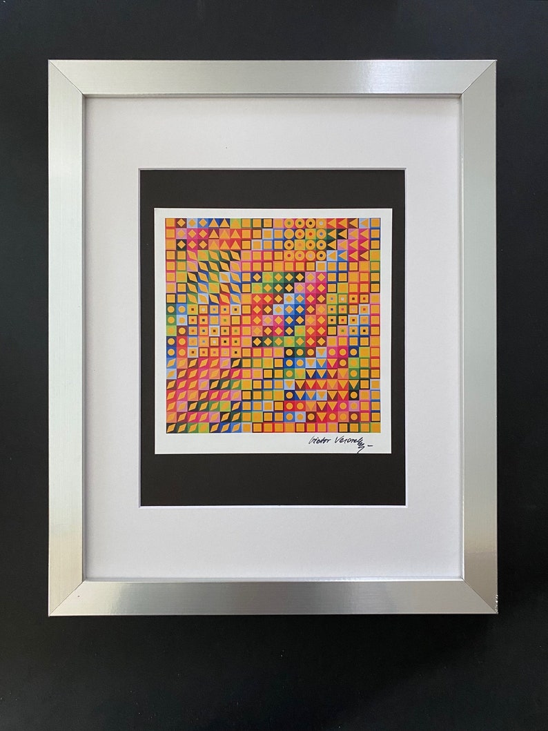 May include: A framed print of a colorful geometric pattern with squares, circles, and triangles. The print is signed "Victor Vasarely" in the bottom right corner.