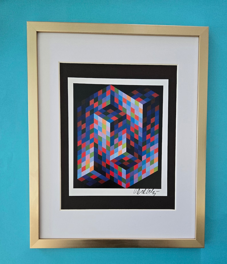 Puede incluir: Una impresi&oacute;n enmarcada de una obra de arte abstracta geom&eacute;trica colorida. La obra de arte es un dise&ntilde;o 3D pixelado multicolor de un cubo. La impresi&oacute;n est&aacute; firmada "Vasarely" en la esquina inferior derecha.
