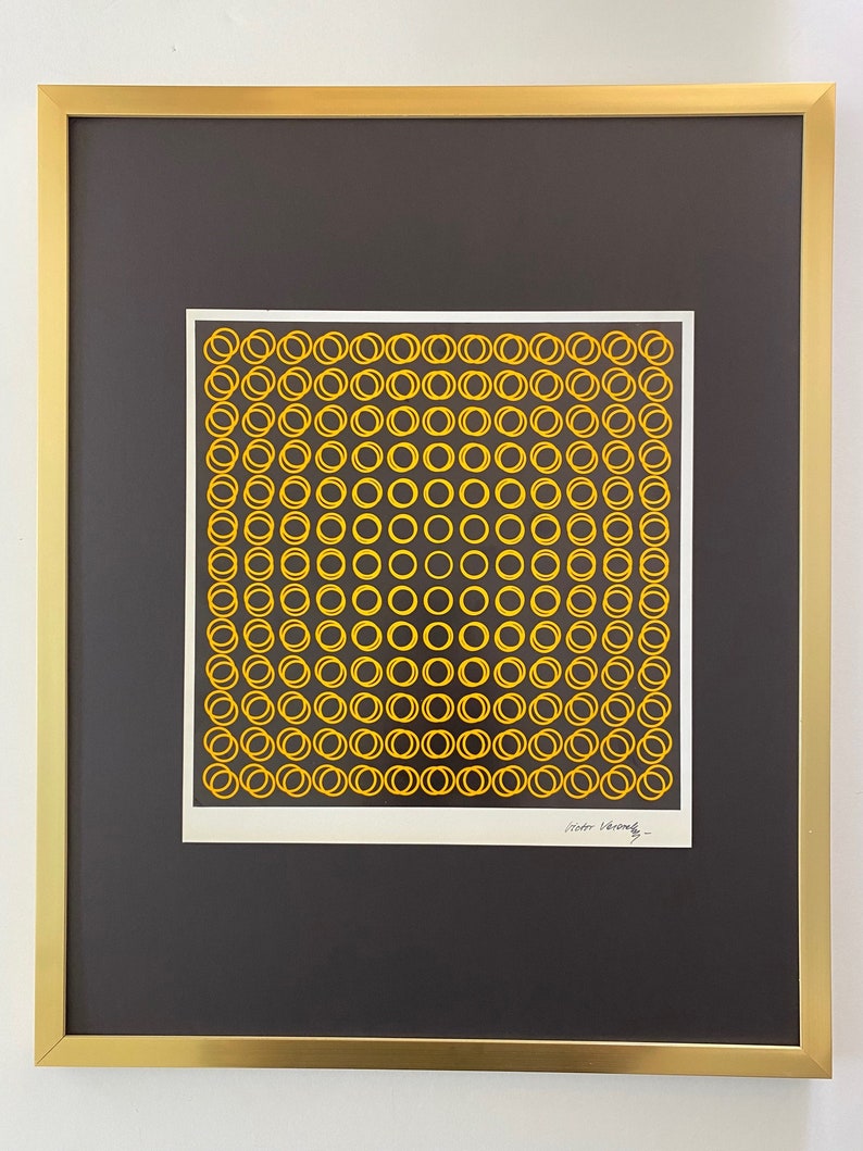 May include: Abstract art print with a repeating pattern of yellow circles on a white background, set against a black mount. The artwork is framed in a gold-coloured metal frame, creating a modern aesthetic.