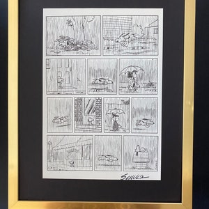 May include: A framed black and white comic strip featuring a series of panels depicting a character in the rain. The artwork is signed "Schulz" in the lower right corner. The frame is gold-colored.