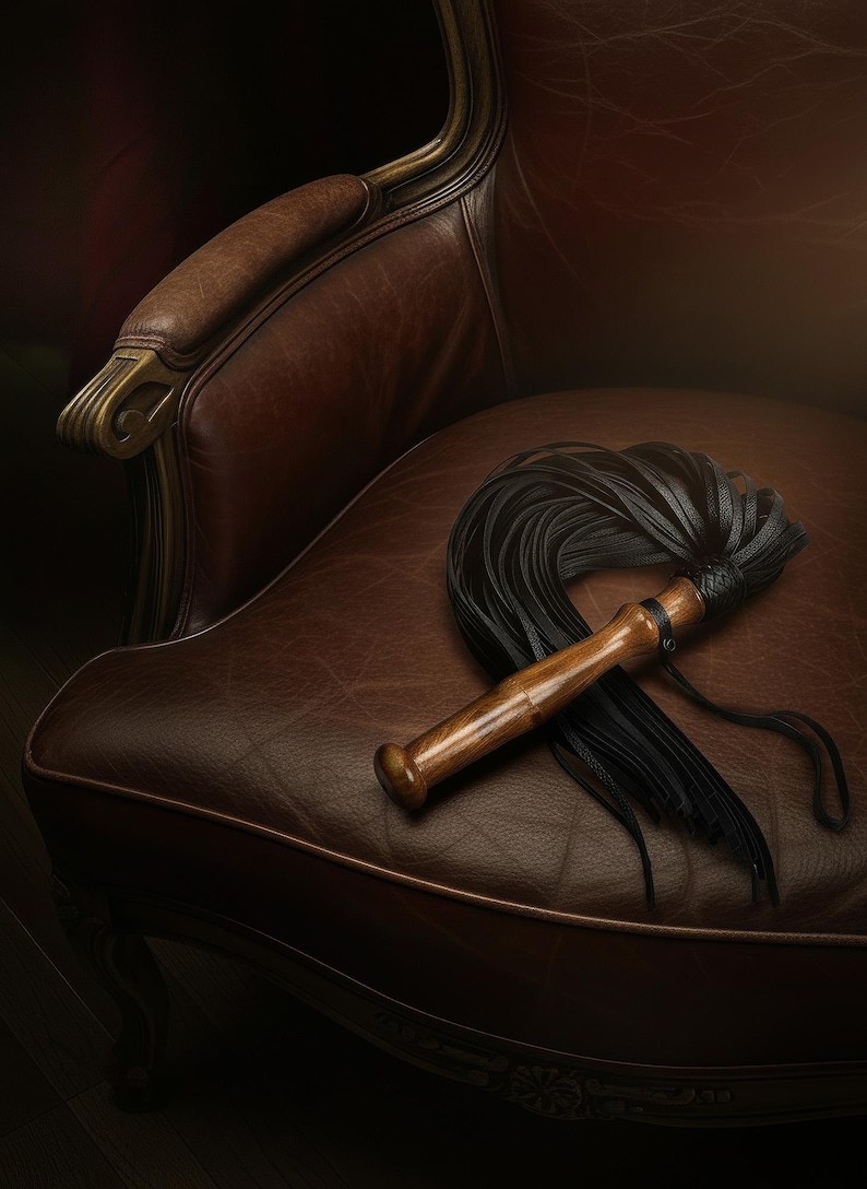 May include: A black leather flogger featuring a smooth, polished wooden handle with a rounded pommel. The handle is connected to a bundle of thin, flexible black leather strips that fan out, secured by a braided leather collar at the base.