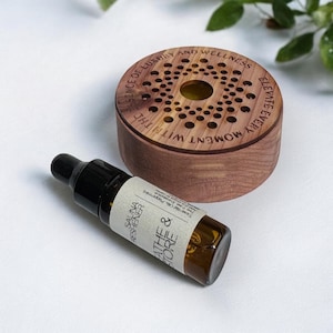 May include: A wooden aromatherapy diffuser with a circular design and the text "ELEVATE EVERY MOMENT WITH THE ESSENCE OF LUXURY AND WELLNESS." Next to it is a small brown glass bottle labeled "Breathe & Store" and "Sauna Freshener."