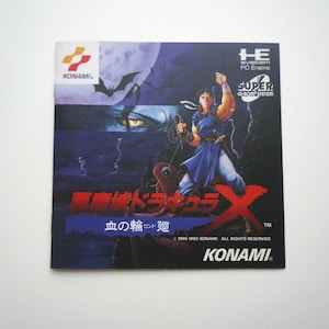 Puede incluir: Un cartucho de videojuego para Super Nintendo Entertainment System (SNES) con un diseño rojo y negro. El juego se llama "悪魔城ドラキュラX" (Akumajō Dracula X) y el subtítulo es "血の輪廻" (Chi no Rinne). El juego es publicado por Konami.