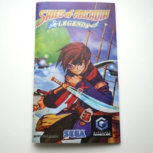 May include: A colorful video game instruction manual cover featuring a character with a sword and an eyepatch. The title of the game is "Skies of Arcadia Legends" and the game is for the Nintendo GameCube. The cover also features the Sega logo.