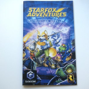May include: A blue and purple video game instruction booklet for Star Fox Adventures for the Nintendo GameCube. The cover features a group of characters from the game, including Fox McCloud, Krystal, and Falco Lombardi.