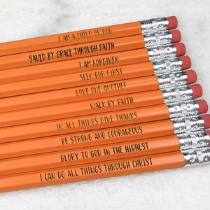 Könnte beinhalten: Ein Satz mit 12 orangen Bleistiften, auf denen inspirierende Zitate gedruckt sind. Die Zitate lauten: "Ich bin ein Kind Gottes", "Gerettet durch Gnade durch Glauben", "Ich bin vergeben", "Suche zuerst Gott", "Liebe einander", "Gehe im Glauben", "Dankt in allen Dingen", "Seid stark und mutig", "Ehre sei Gott in der Höhe", und "Ich kann alles durch Christus tun".